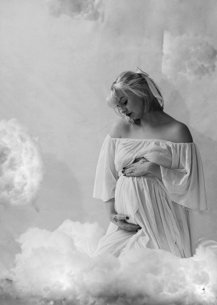 Black and white portrait of pregnant woman in white dress among clouds.