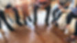 Diverse group sitting in a circle, engaged in discussion, wooden floor. Focus on hands and