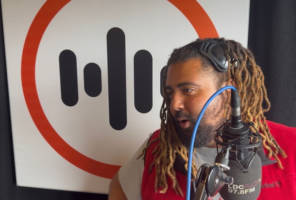 Man with dreadlocks speaking into a studio microphone, with an LBC Radio 97.8 FM logo behind him.