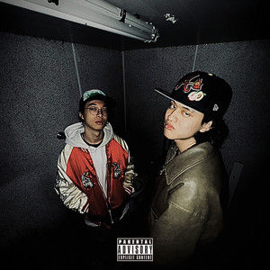 Two young men pose in a dark studio, one in a red jacket, one in a leather jacket and cap; Parental Advisory label.