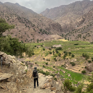 The Guide(Radouane) walking along a narrow trail overlooking green terraced fields and Berber villages in the High Atlas Mountains near Azzaden, Morocco