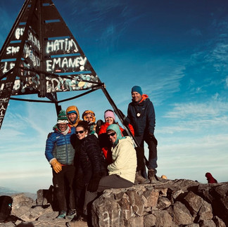 Group of trekkers at the summit of Mount Toubkal with the summit marker in the Atlas Mountains