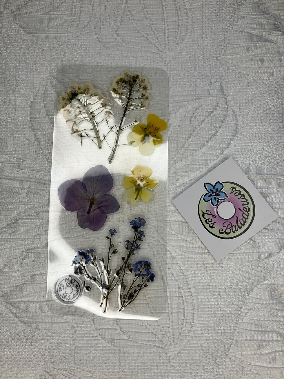 Marque-page fleuri avec fleurs pressées et le logo Les Baladeuses posé à côté.