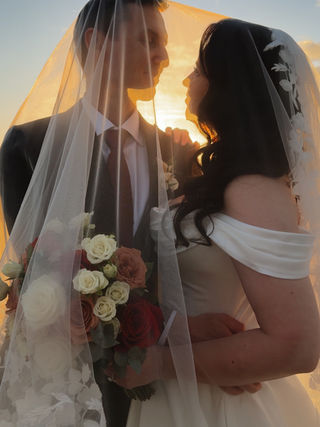 Bride and groom sharing a sunset moment beneath a wedding veil.
