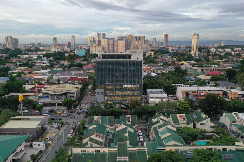 Abenson Design Center in San Juan City stands out as a modern architectural landmark. This aerial view showcases the building's prominent presence in the urban landscape, with a backdrop of the Manila skyline. The design reflects a contemporary interpretation of Philippine architectural principles, creating a visually striking and functional commercial space.