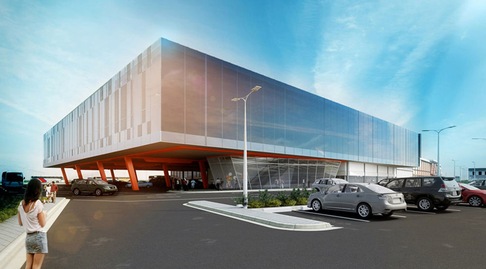 The modern building, echoing Philippine architecture, features a large overhanging structure supported by orange pillars. In the foreground, a bustling parking lot accompanies the Bataan Terminal. A person stands on the left, gazing up at the structure against a clear sky dotted with clouds.