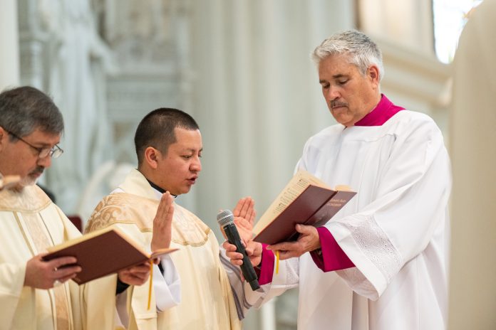 Fr. Patricio Chuquimarca reads during the Liturgy of the Eucharist as Deacon Robert Rinne holds the book of Eucharistic Prayers during his priest ordination. (Photo by Daniel Petty/Denver Catholic)
