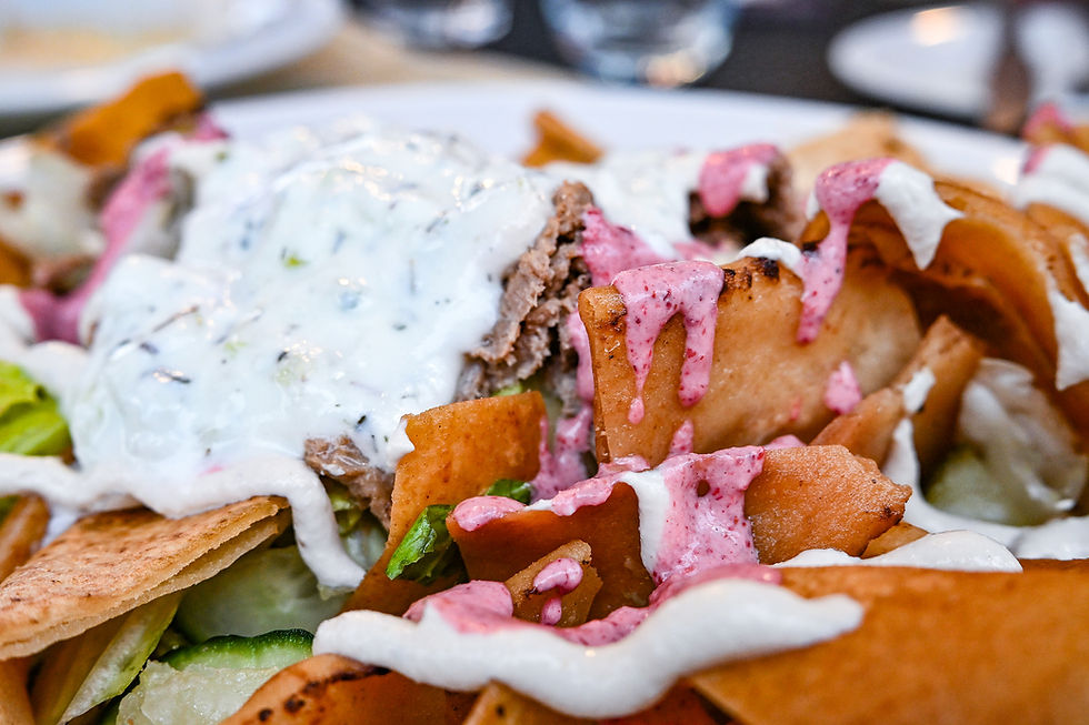 Close-up of a dish with pita chips drizzled in white and pink sauces, featuring a creamy topping on mixed greens. Vibrant and appetizing.