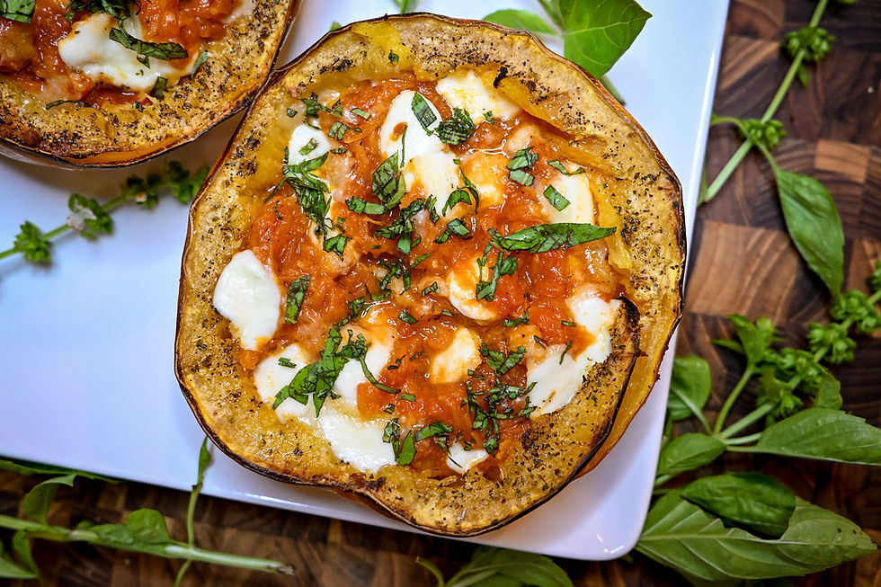 Roasted spaghetti squash halves topped with tomato sauce, melted mozzarella, and basil on a white plate with fresh herbs.