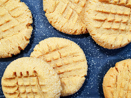 Peanut butter cookies on a dark surface with sugar sprinkled around. Cookies are golden with forked crosshatch patterns, creating a cozy feel.