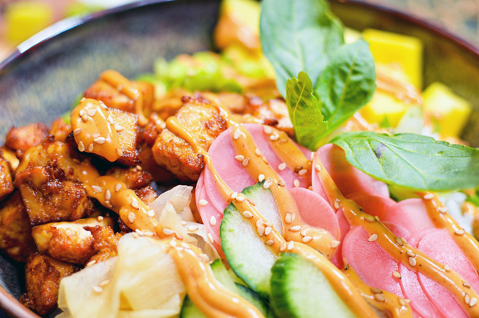 A colorful bowl of tofu, pink radishes, cucumbers, and fresh greens drizzled with sauce, topped with sesame seeds, creating a vibrant dish.