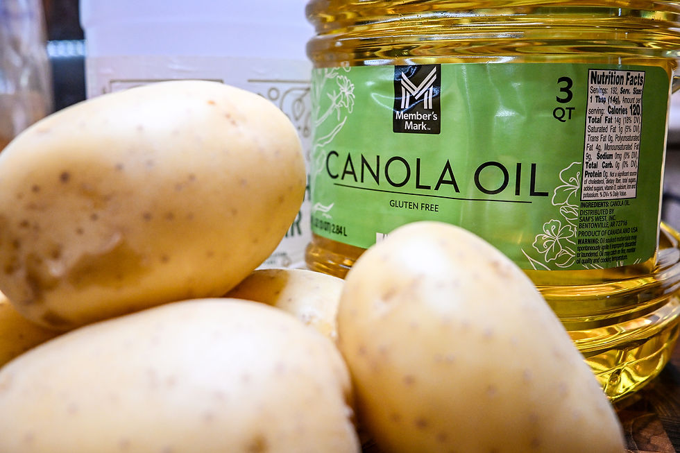 Close-up of potatoes beside a Member’s Mark canola oil jug labeled 3 QT and gluten free, on a kitchen counter.
