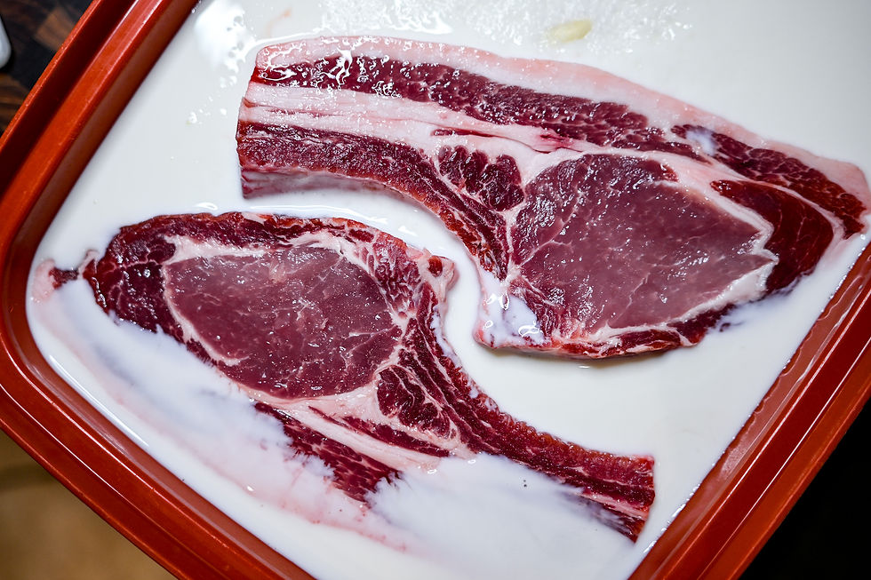 Two raw steaks marinating in a white liquid, likely milk, placed in a red tray. The steaks are vibrant red and white.