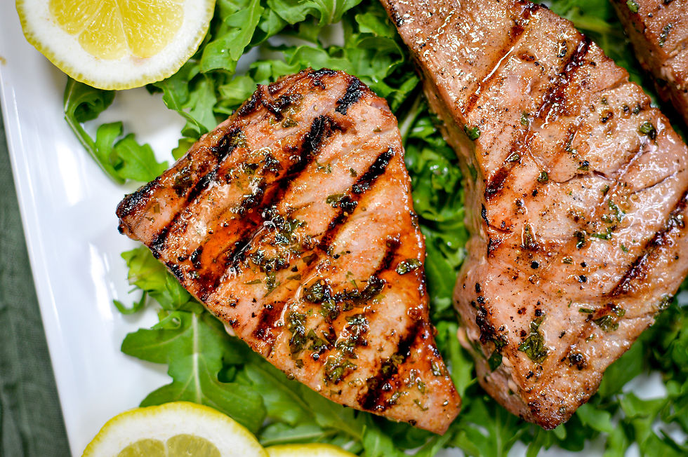 Grilled tuna steaks on fresh arugula with lemon slices. The salmon is garnished with herbs and has distinct grill marks.