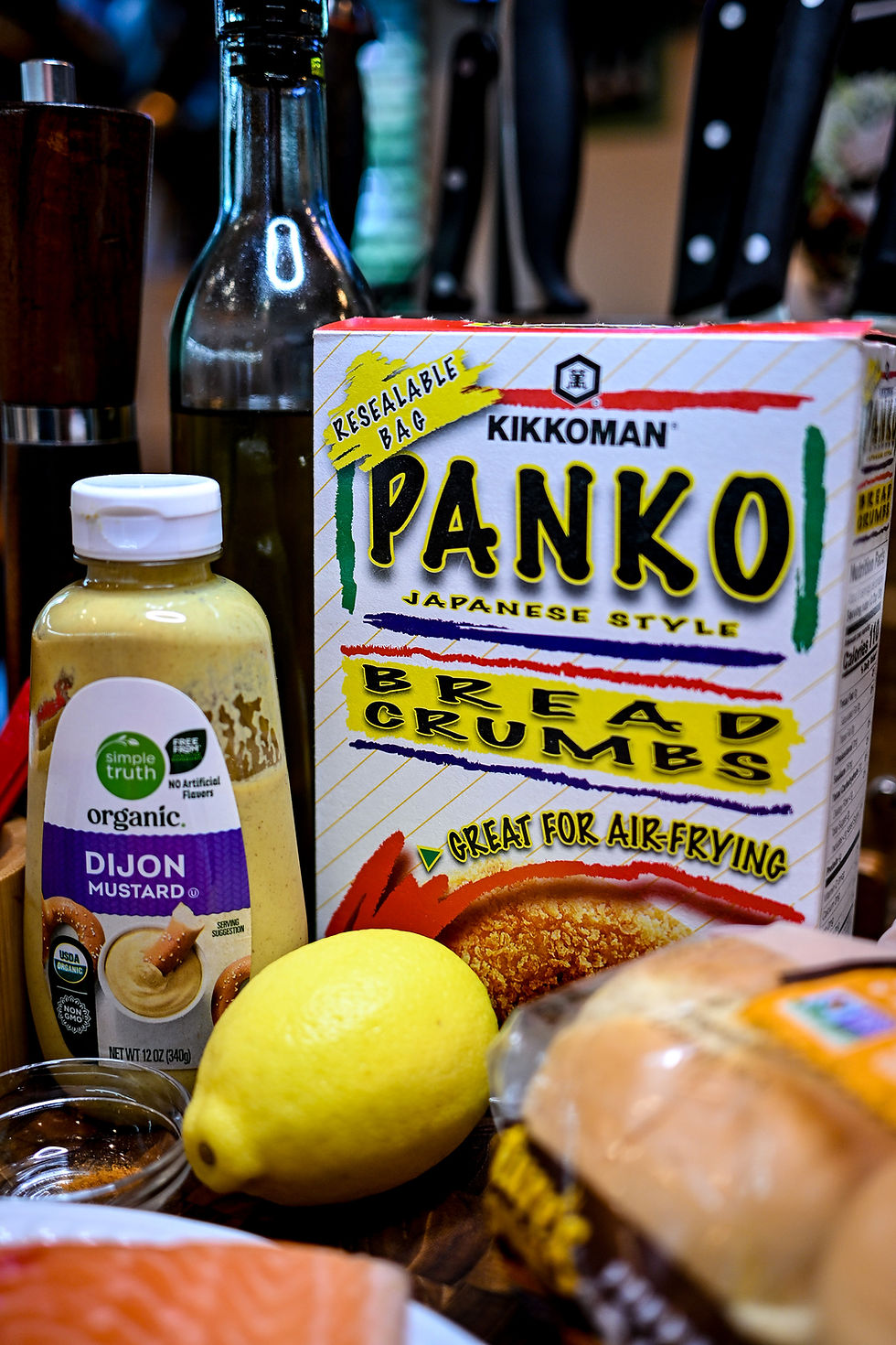 Kikkoman Panko breadcrumbs box with a yellow highlight, organic Dijon mustard, and a lemon on a kitchen counter, suggesting meal prep.