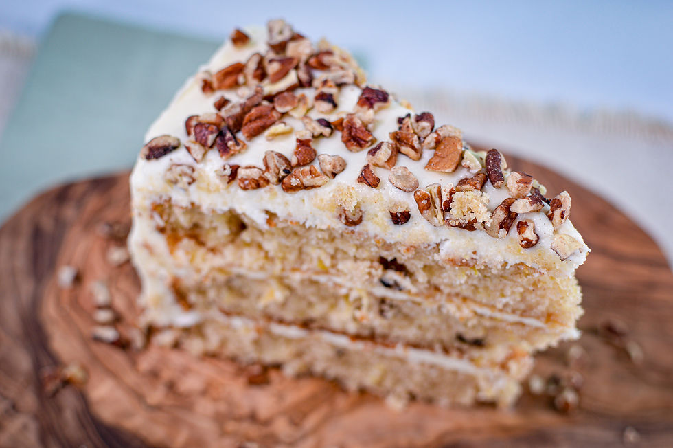 Slice of layered cake topped with chopped pecans and cream, on a wooden board. Soft, neutral colors create a cozy atmosphere.