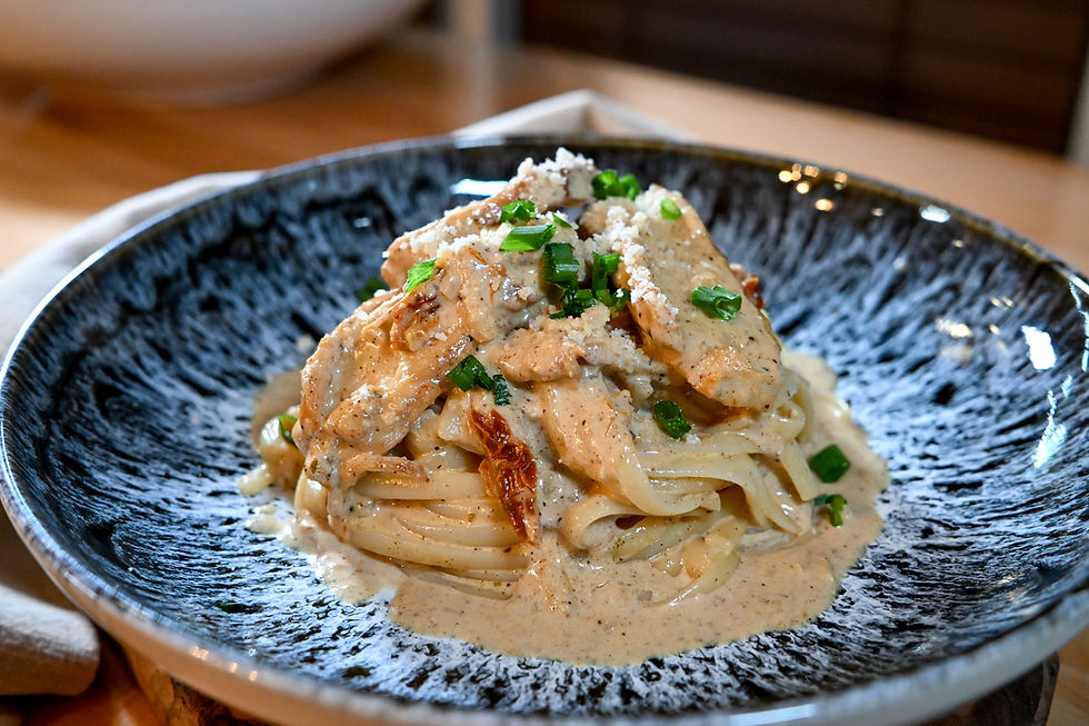 A black bowl with creamy pasta topped with grilled chicken, green onions, and grated cheese. Wooden table background adds a warm feel.