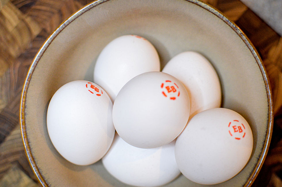 Bowl of white eggs marked with red "EB" on a wooden table. Eggs are neatly arranged, creating a clean and natural look.