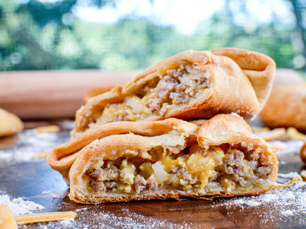 Two halves of a savory pastry filled with meat and cheese on a wooden surface, surrounded by flour and cheese shreds. Rustic, appetizing scene.