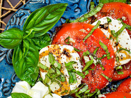 Caprese salad on a blue floral plate with sliced tomatoes, mozzarella, basil, and balsamic drizzle. Fresh, vibrant colors create a lively mood.