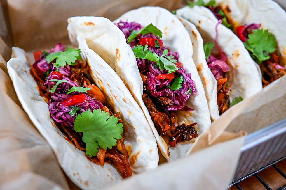 Tray of soft tacos filled with shredded meat, purple slaw, red peppers, and cilantro on parchment paper in a food close-up