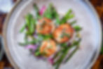 Seared scallops with basil on sautéed asparagus and red onions, served on a gray plate. The vibrant vegetables add a fresh touch.