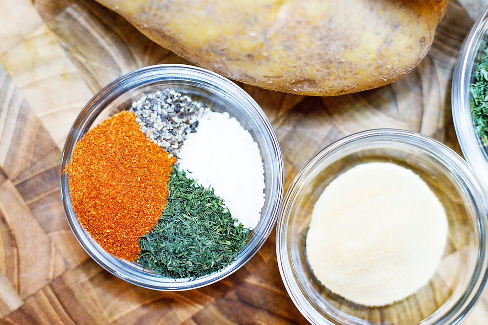 Bowls with red, green, black, and white spices on a wooden surface next to a potato. Bright colors create a vibrant cooking scene.