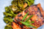 Grilled salmon topped with green onions, sesame seeds, served on a plate with roasted broccoli. Bright and appetizing presentation.
