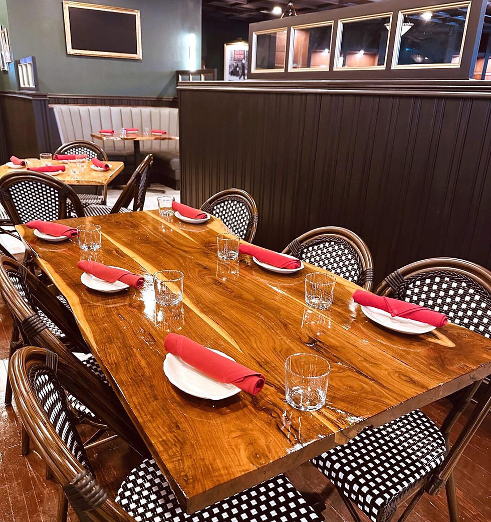 Wooden table set for dining with red napkins, white plates, and glasses. Checkered chairs surround the table in a cozy restaurant.