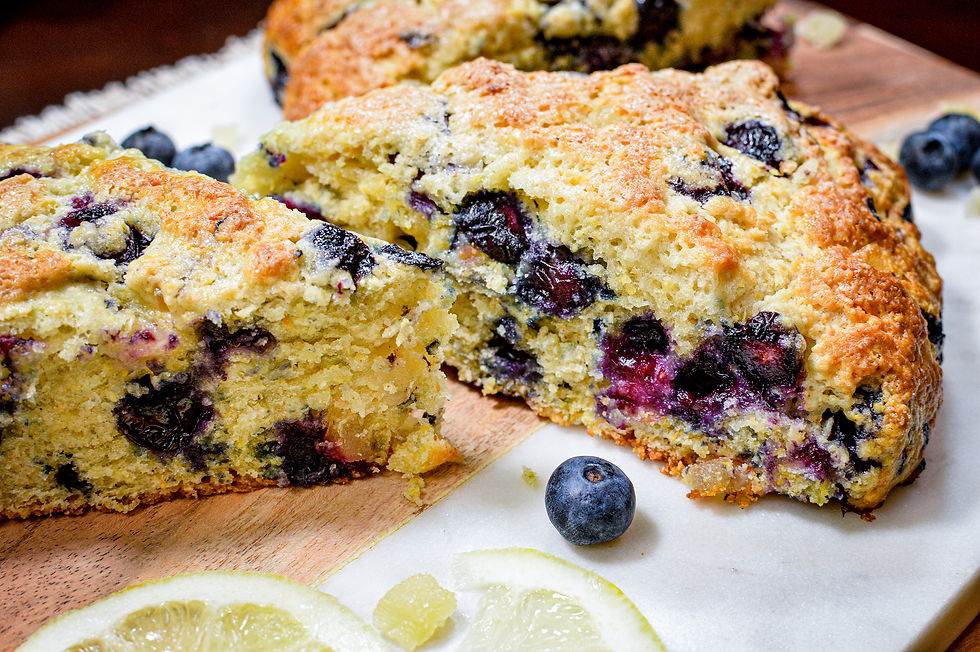 Close-up of blueberry scones on a wooden board, golden brown with purple berry spots. Blueberries and lemon slices are scattered around.