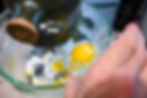 Close-up of a hand cracking an egg into a glass bowl while an electric mixer blends the batter.