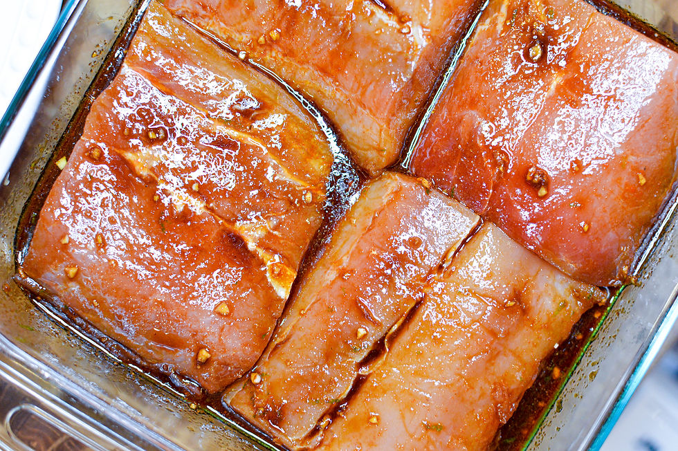 Four marinated salmon fillets in a glass dish, coated with a glossy, brown sauce and visible garlic pieces, ready for cooking.