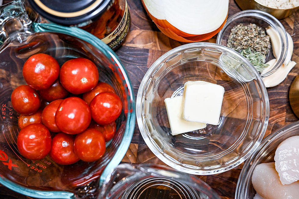 Cherry tomatoes in a measuring cup, butter in a bowl, onion, garlic, herbs, scallops on a wooden surface. Cozy cooking mood.