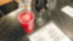 Drinks on a dark table: a glass of red juice, red wine, and water with ice. Menus titled Fernbank are visible. Cozy dining ambiance.