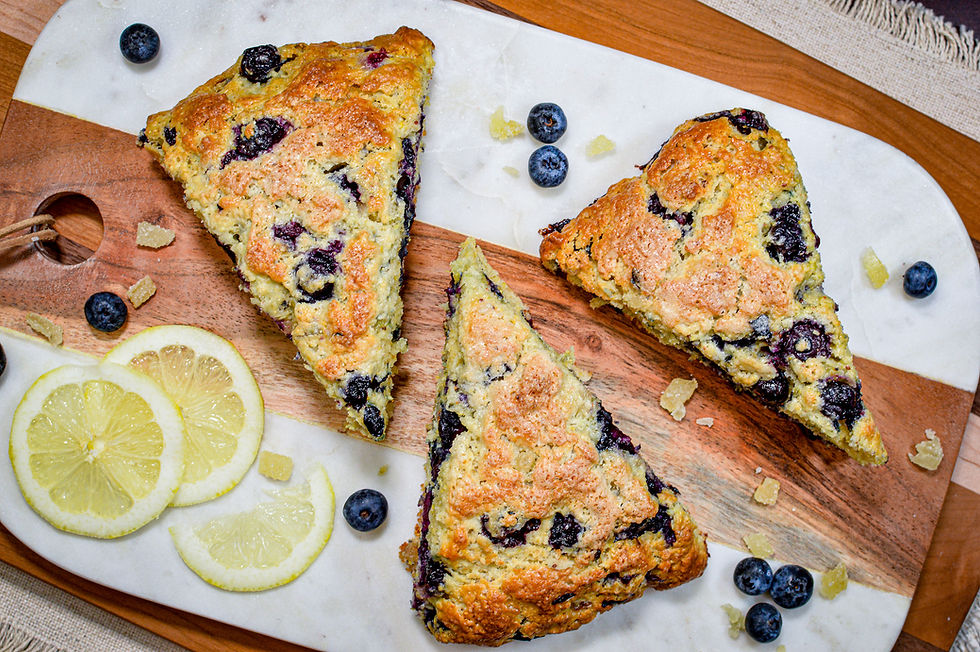 Blueberry scones on a wooden board with lemon slices and blueberries. The golden scones are set against a white marble background.