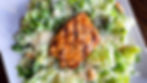 Grilled salmon on romaine lettuce with parmesan and croutons, served on a white plate. Vibrant greens and a rustic brown tabletop.