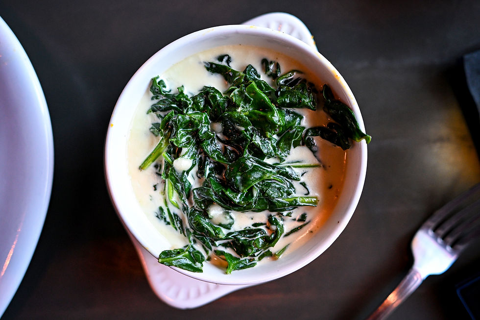 Bowl of creamy spinach on a dark table, surrounded by a fork and a partial view of a white plate. Rich green and white contrast.