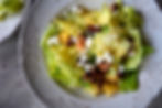 A decorative plate of salad with lettuce, pecans, peaches, and feta, topped with vinaigrette, on a textured marble surface.