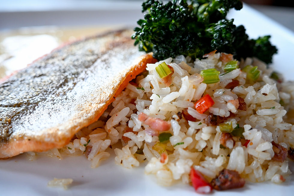 Grilled fish fillet with crispy skin, served with colorful vegetable rice and a side of leafy greens on a white plate.