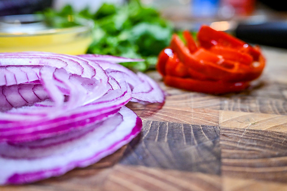 Sliced red onion in foreground with chopped tomato, greens, and a bowl of dressing on a wooden cutting board, colorful and fresh