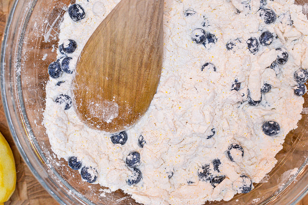 Wooden spoon in flour with blueberries in a glass bowl on a wooden surface. Visible lemon adds a fresh, baking mood.