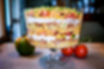 Layered taco dip in a glass bowl with beans, cheese, corn, tomatoes, and sour cream on a kitchen counter