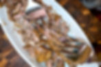 Shredded roast meat in a white serving dish, with two metal forks and spoons on a wooden table.