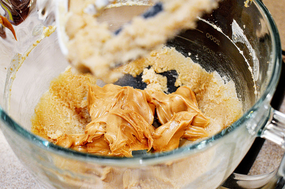 Peanut butter and sugar are mixed in a glass bowl on a countertop. The mixture is creamy with a light brown color.