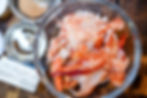 Fresh lobster meat in a clear bowl on a wooden surface, surrounded by ingredients like sand-colored seasoning and a stick of butter.