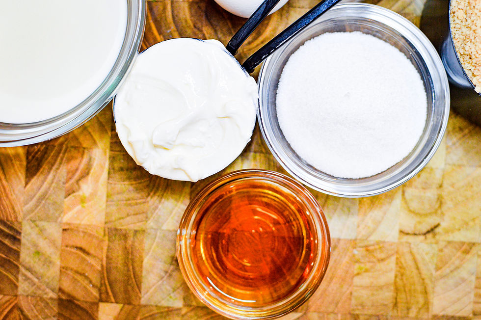 Ingredients on a wooden board: glass bowls with milk, cream, sugar, and honey. Light colors on a patterned wooden background.