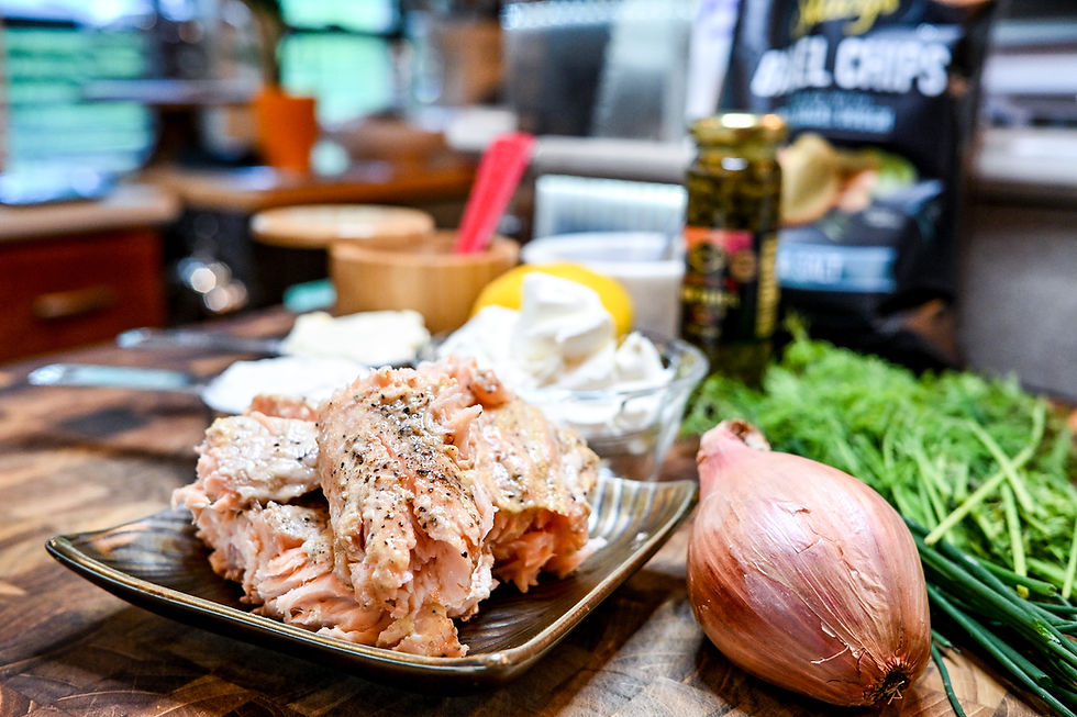 Raw salmon on a plate with a shallot, chives, and herbs on a wooden counter, with blurred spice jars in the background.