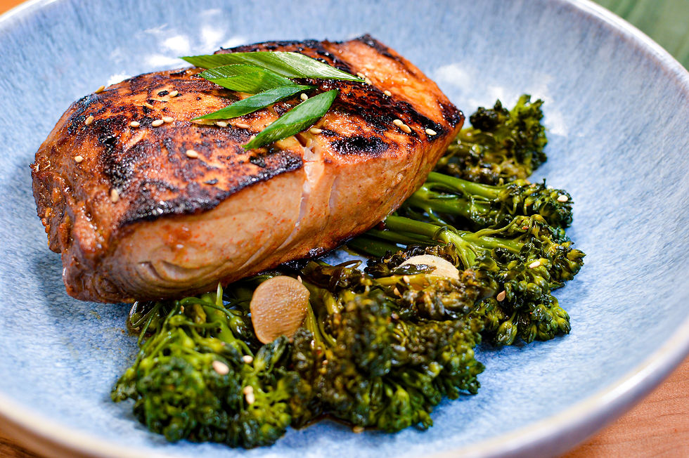Grilled salmon fillet with sesame seeds and green garnish on a bed of broccolini, served on a blue plate, creating a fresh, appetizing look.