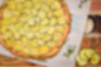 Zucchini tart with golden slices on parchment paper, garnished with herbs on a wooden board. Earthy tones create a rustic vibe.