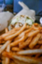 A wrapped chicken gyro with lettuce and sauce beside a mound of golden-brown fries on a dark tray, suggesting a casual dining setting.